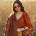 Ragazza con camicia arancione, gonna giallo ocra e cappotto marrone