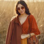 Ragazza con camicia arancione, gonna giallo ocra e cappotto marrone