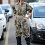 Donna indossa tuta jumpsuit con stampa pitonata, occhiali da sole e stivali neri con tacco alto