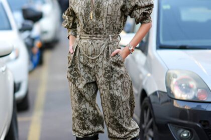 Donna indossa tuta jumpsuit con stampa pitonata, occhiali da sole e stivali neri con tacco alto