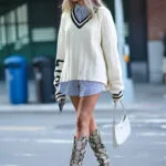 Ragazza bionda indossa maxi maglione con scollo a V, lunga camicia a righe e stivali animalier
