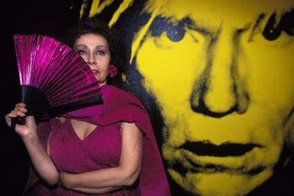 L'artista Ultraviolet con vestito e ventaglio viola è davanti a una grande foto di Andy Warhol