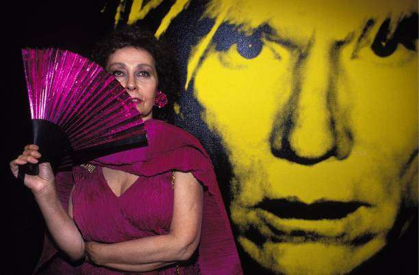 L'artista Ultraviolet con vestito e ventaglio viola è davanti a una grande foto di Andy Warhol