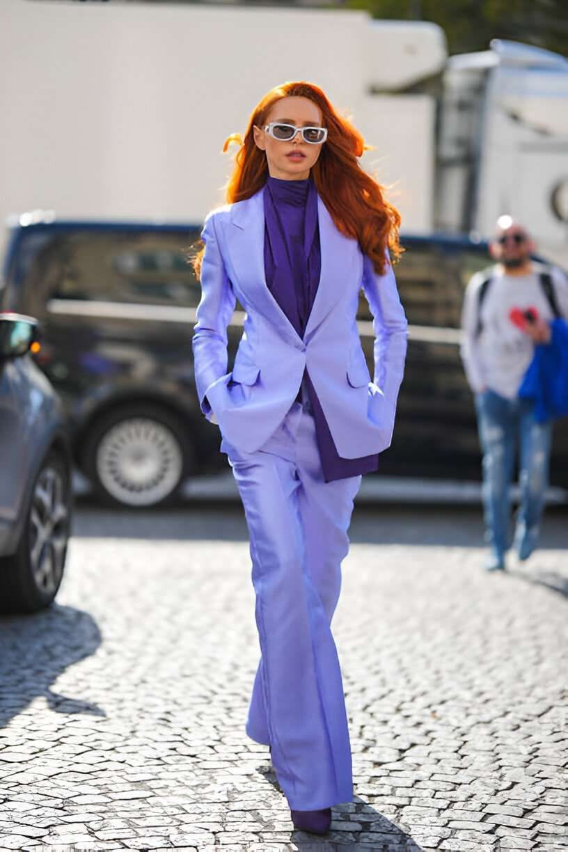 Una ragazza con i capelli rossi indossa camicia viola intenso e un completo viola più chiaro
