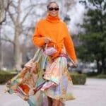 Donna indossa gonna lunga di tendenza a balze colorata, maglia arancione e occhiali da sole