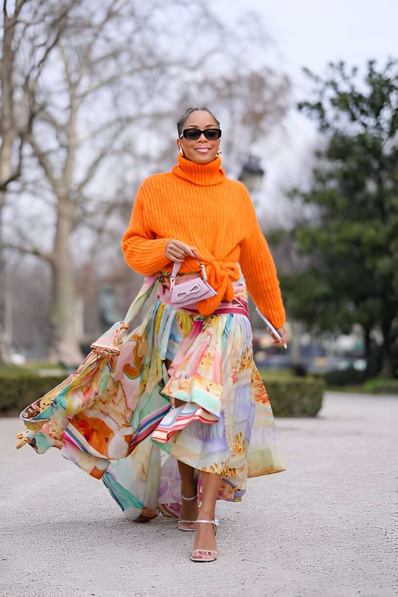 Donna indossa gonna lunga di tendenza a balze colorata, maglia arancione e occhiali da sole