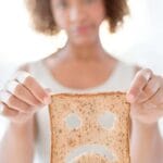 Simbolo dell'intolleranza al glutine: Una donna mostra una fetta di pane con intagliati occhi e bocca triste
