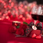 Simboli di San Valentino: due calici con vino rosso, candela accesa, tovaglia rossa e pacchetto con cuoricino