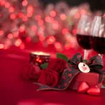 Simboli di San Valentino: due calici con vino rosso, candela accesa, tovaglia rossa e pacchetto con cuoricino