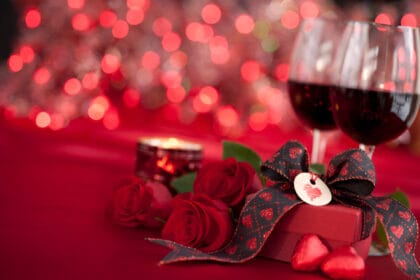 Simboli di San Valentino: due calici con vino rosso, candela accesa, tovaglia rossa e pacchetto con cuoricino