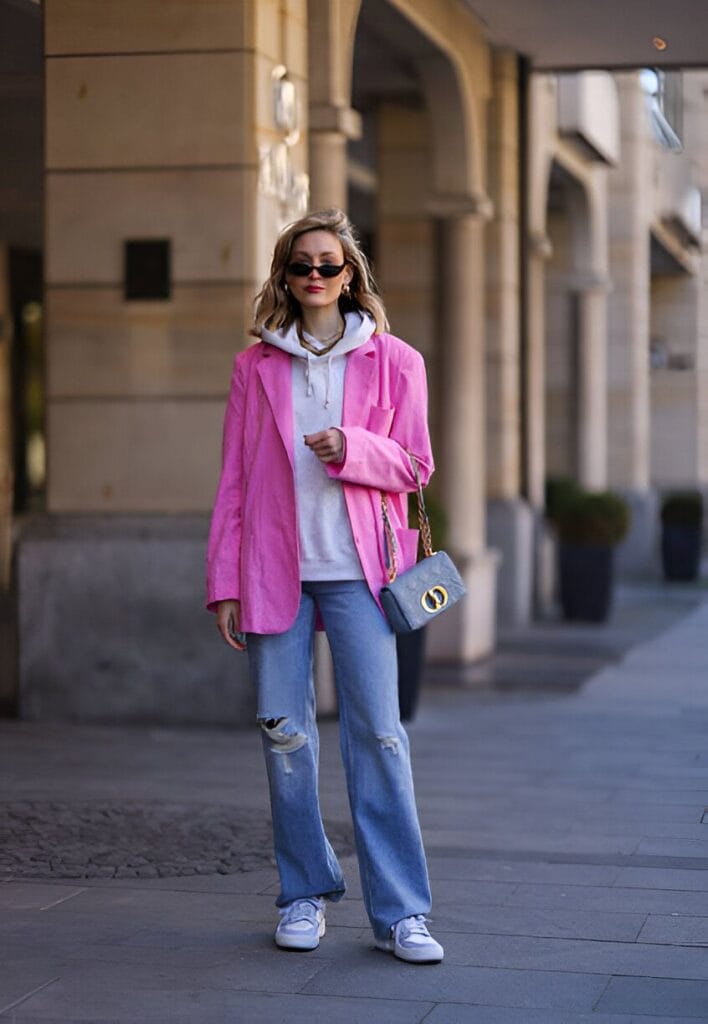 Outfit primaverile composto da jeans, blazer destrutturato rosa acceso e felpa con cappuccio