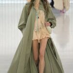 Modella indossa trench lungo verde salvia e minidress rosa cipria, outfit classico moda primaverile