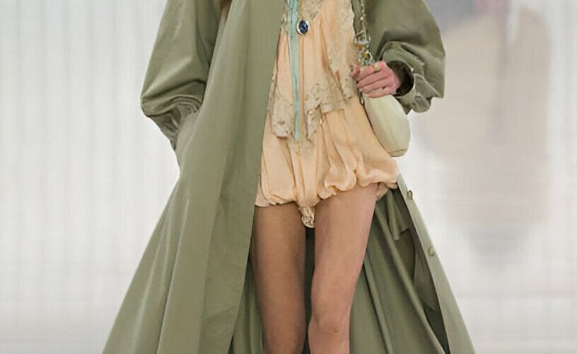 Modella indossa trench lungo verde salvia e minidress rosa cipria, outfit classico moda primaverile
