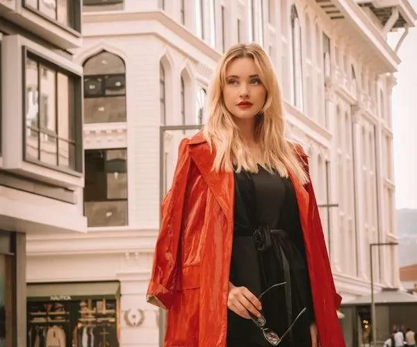 Ragazza con vestito nero e trench corallo. Un outfit chic che può essere creato senza spendere soldi