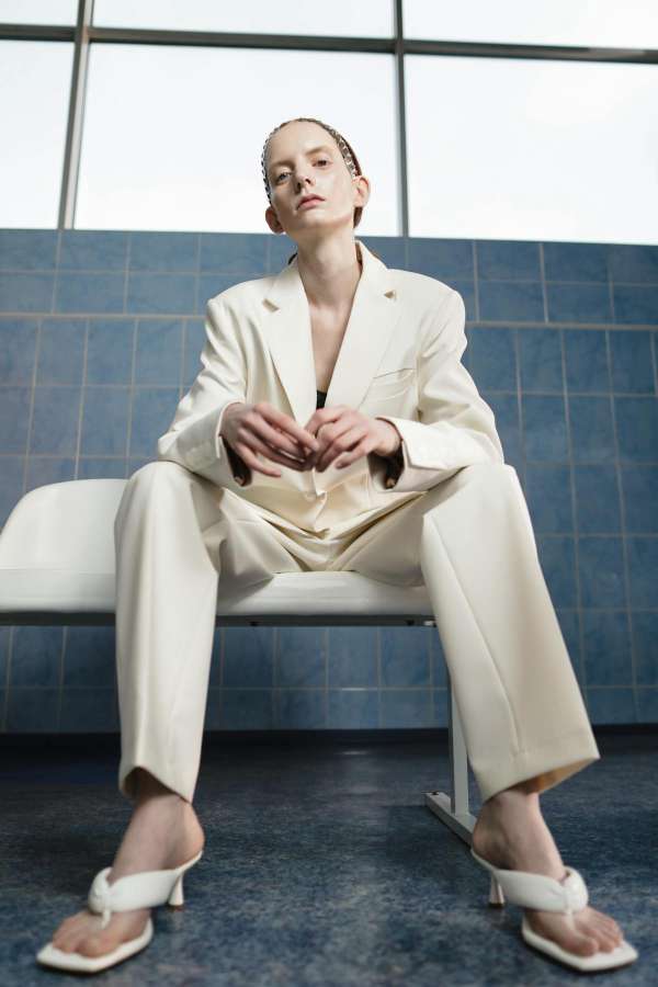 Ragazza seduta indossa un tailleur nel colore neutro bianco panna e sandali infradito bianchi