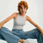 Ragazza indossa un modello di jeans bootcut, canotta bianca e sneakers.