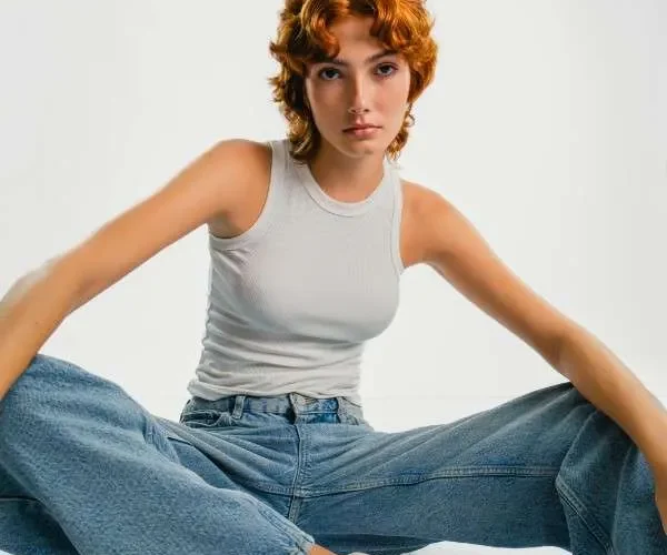 Ragazza indossa un modello di jeans bootcut, canotta bianca e sneakers.