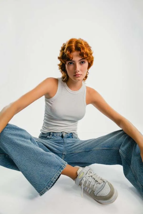 Ragazza indossa un modello di jeans bootcut, canotta bianca e sneakers.
