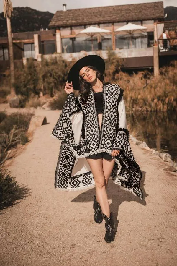 Donna con poncho bianco e nero a motivi geometrici e bordo a frange