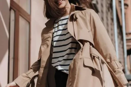 Ragazza sorridente con trench beige, maglietta a righe e berretto nero. Outfit casual chic da mezza stagione.
