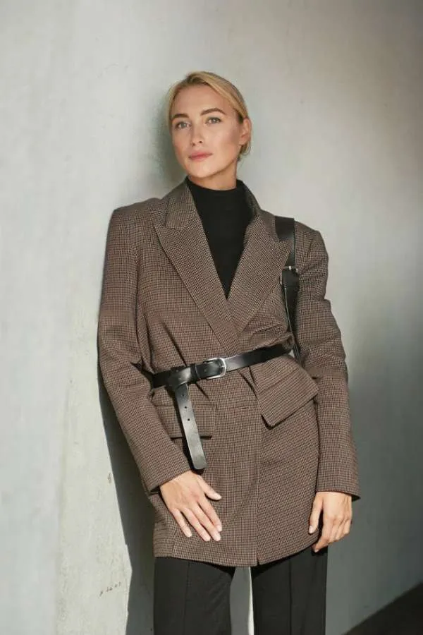 Una donna indossa un blazer oversize marrone stretto in vita da una cintura in pelle nera.