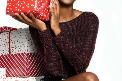 Donna sorride felice seduta tra i regali di Natale e tiene un pacco rosso in mano