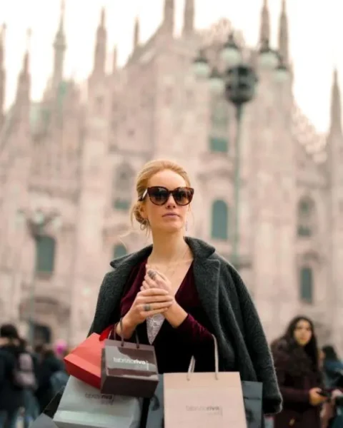 Donna elegante con borse di boutique a Milano: esempio di shopping consapevole e di qualità durante i saldi.