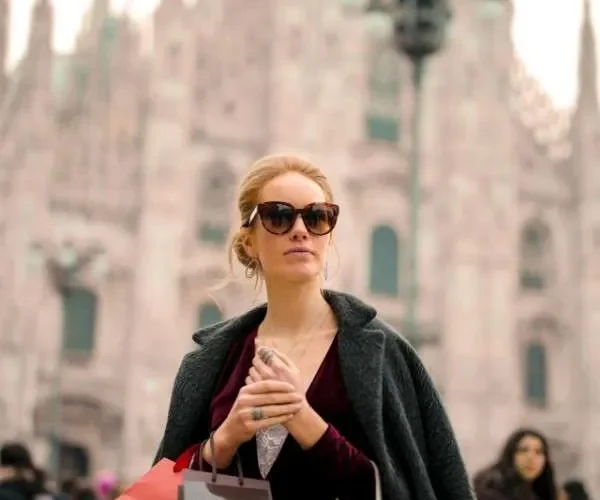 Donna elegante con borse di boutique a Milano: esempio di shopping consapevole e di qualità durante i saldi.
