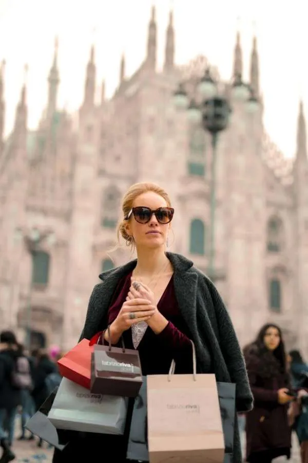 Donna elegante con borse di boutique a Milano: esempio di shopping consapevole e di qualità durante i saldi.
