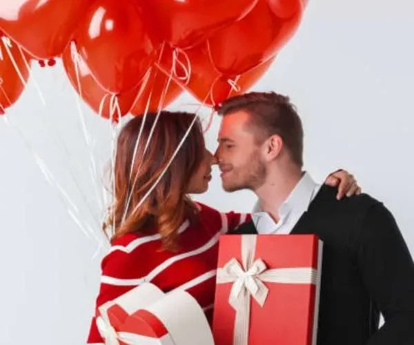 Idee regalo San Valentino: coppia felice con pacchetti regalo e palloncini a cuore.