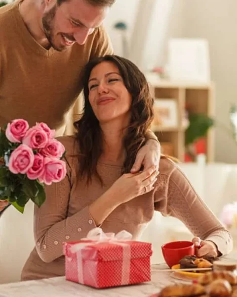 Coppia festeggia San Valentino con rose rosa e pacchetto regalo rosso a tavola