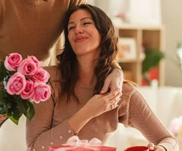 Coppia festeggia San Valentino con rose rosa e pacchetto regalo rosso a tavola