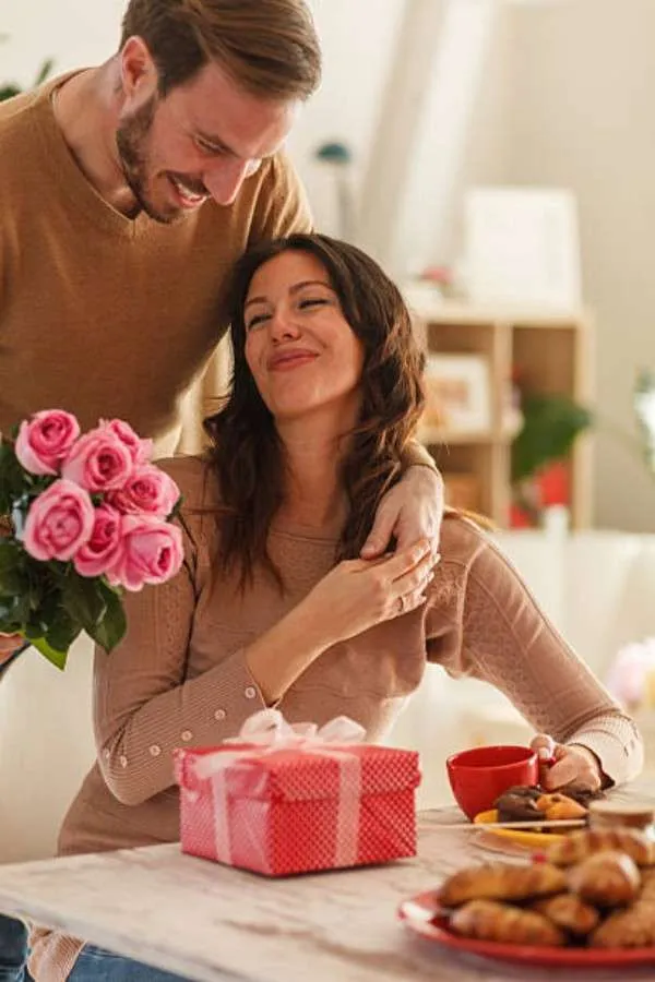 Coppia festeggia San Valentino con rose rosa e pacchetto regalo rosso a tavola