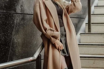 Donna bionda con cappotto lungo color cammello e stivali neri, esempio di stile sofisticato e capospalla di alta qualità