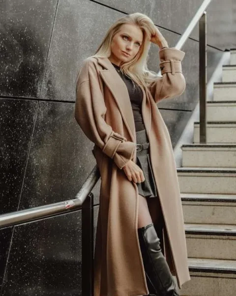 Donna bionda con cappotto lungo color cammello e stivali neri, esempio di stile sofisticato e capospalla di alta qualità