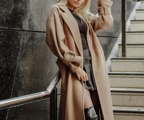 Donna bionda con cappotto lungo color cammello e stivali neri, esempio di stile sofisticato e capospalla di alta qualità