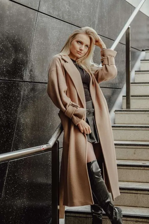 Donna bionda con cappotto lungo color cammello e stivali neri, esempio di stile sofisticato e capospalla di alta qualità