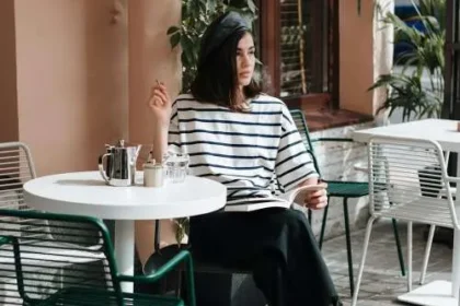 Ragazza seduta a un café indossa un outfit che rappresenta lo stile parigino