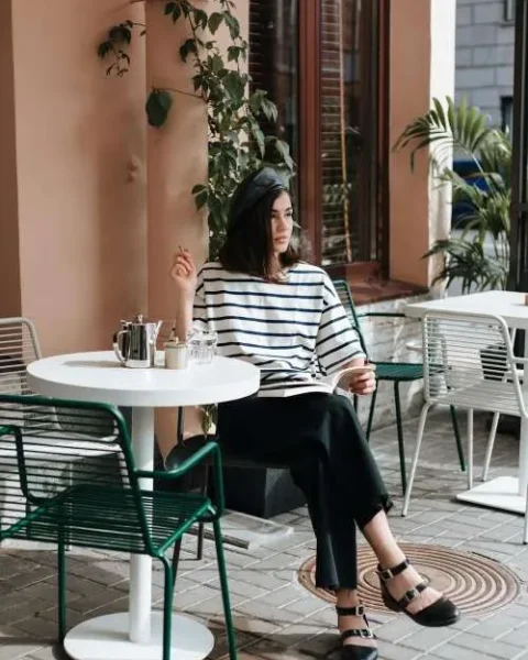 Ragazza seduta a un café indossa un outfit che rappresenta lo stile parigino