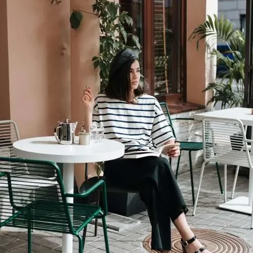 Ragazza seduta a un café indossa un outfit che rappresenta lo stile parigino