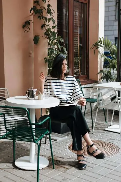 Ragazza seduta a un café indossa un outfit che rappresenta lo stile parigino
