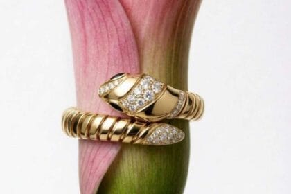 Primo piano di un anello Bulgari Serpenti in oro giallo e diamanti avvolto attorno a una calla rosa, simbolo di lusso ed eleganza senza tempo.