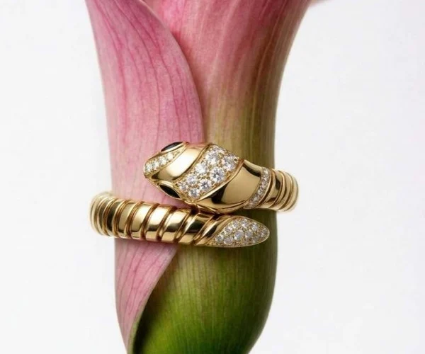 Primo piano di un anello Bulgari Serpenti in oro giallo e diamanti avvolto attorno a una calla rosa, simbolo di lusso ed eleganza senza tempo.