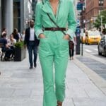 Donna indossa una tuta jumpsuit verde menta con pantaloni capri svasati, abbinata ad accessori bordeaux e sandali alla schiava in un contesto metropolitano.