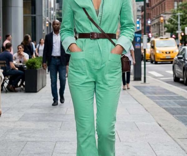 Donna indossa una tuta jumpsuit verde menta con pantaloni capri svasati, abbinata ad accessori bordeaux e sandali alla schiava in un contesto metropolitano.