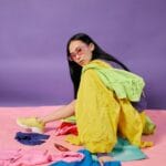 Ragazza seduta circondata da abiti di diversi colori mentre studia gli abbinamenti per un outfit armonioso.