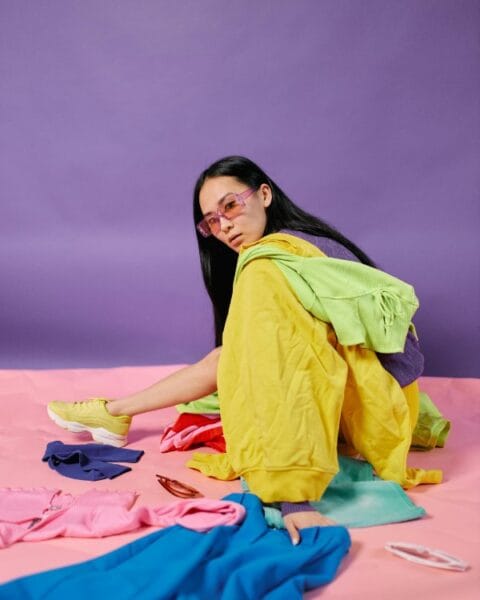 Ragazza seduta circondata da abiti di diversi colori mentre studia gli abbinamenti per un outfit armonioso.