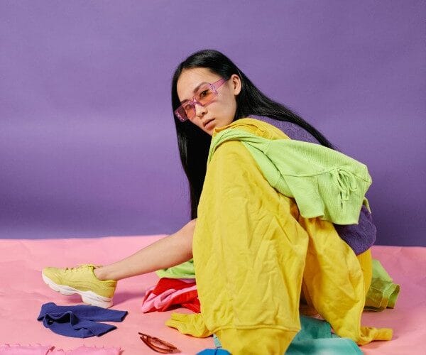 Ragazza seduta circondata da abiti di diversi colori mentre studia gli abbinamenti per un outfit armonioso.