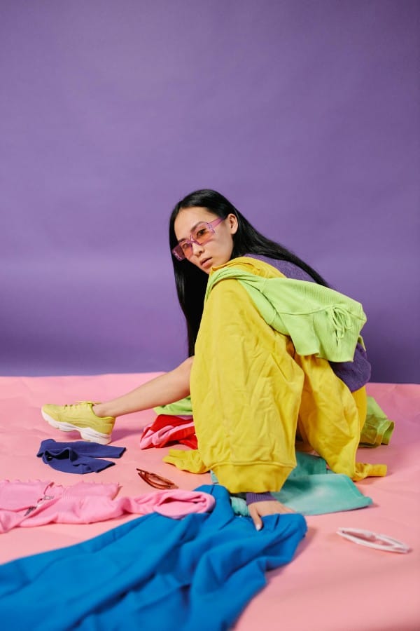 Ragazza seduta circondata da abiti di diversi colori mentre studia gli abbinamenti per un outfit armonioso.