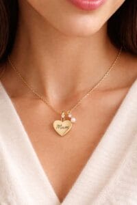 Primo piano di una donna che indossa una sottile catenina d'oro con un ciondolo a forma di cuore con l'incisione "Mum". Idea regalo festa della mamma per Nice to be Woman